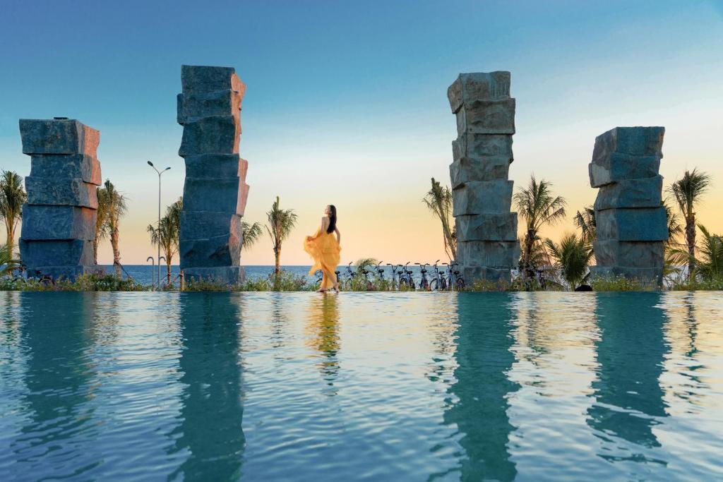 a woman in a dress standing in the water in front of columns at Perolas Villas Resort Powered by ASTON in Phan Thiet