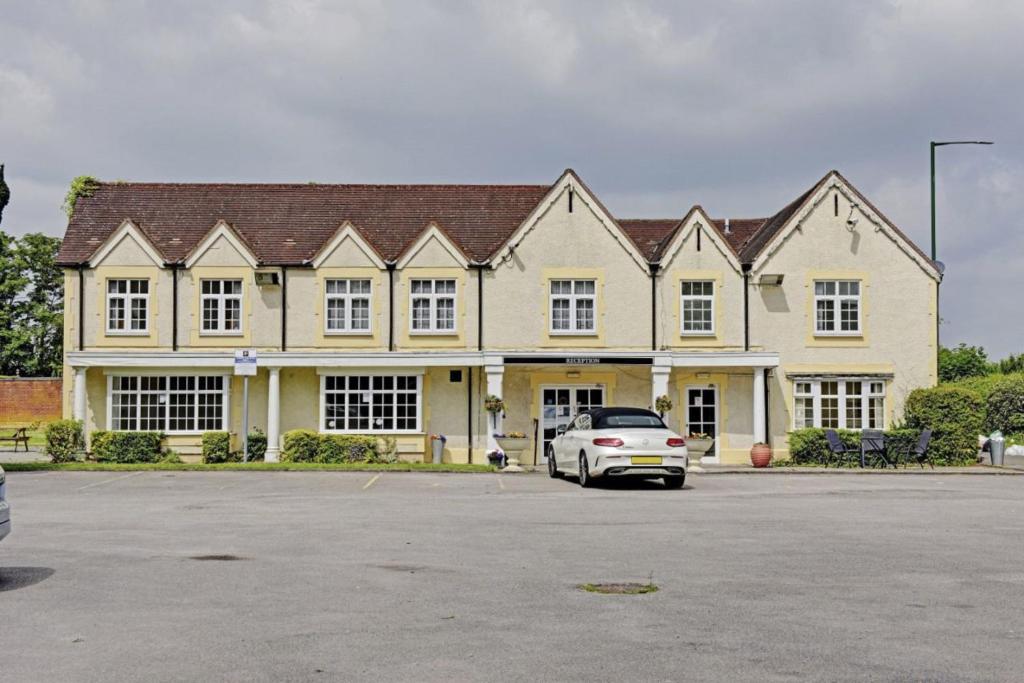 ein weißes Auto, das vor einem großen Haus parkt in der Unterkunft The Gables Hotel, Birmingham Airport in Bickenhill