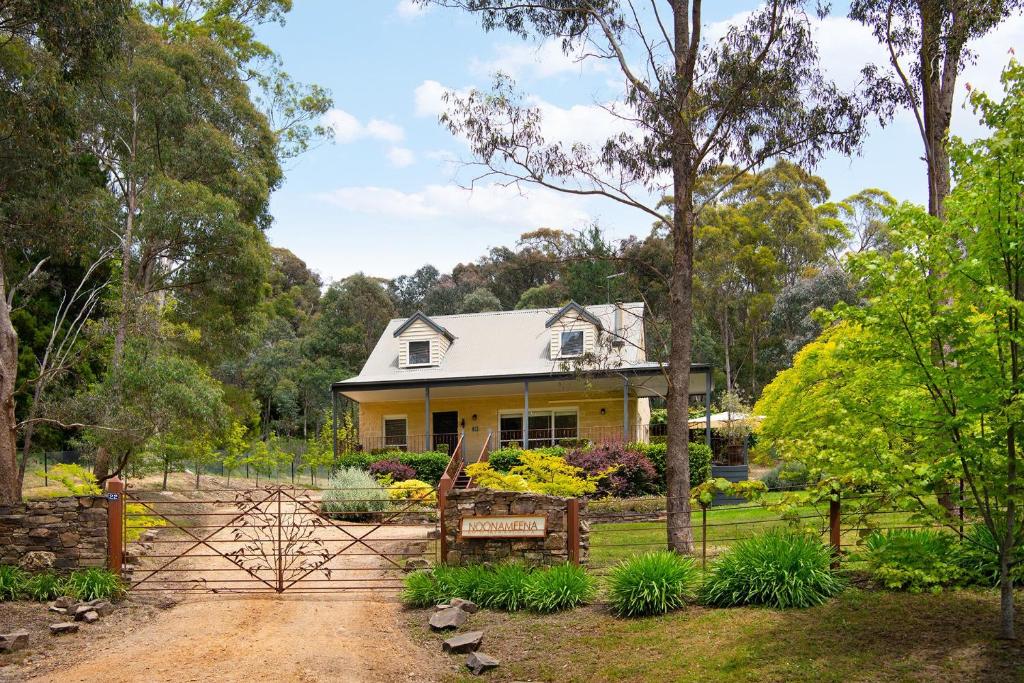 una casa amarilla con una valla y árboles en Noonameena en Hepburn
