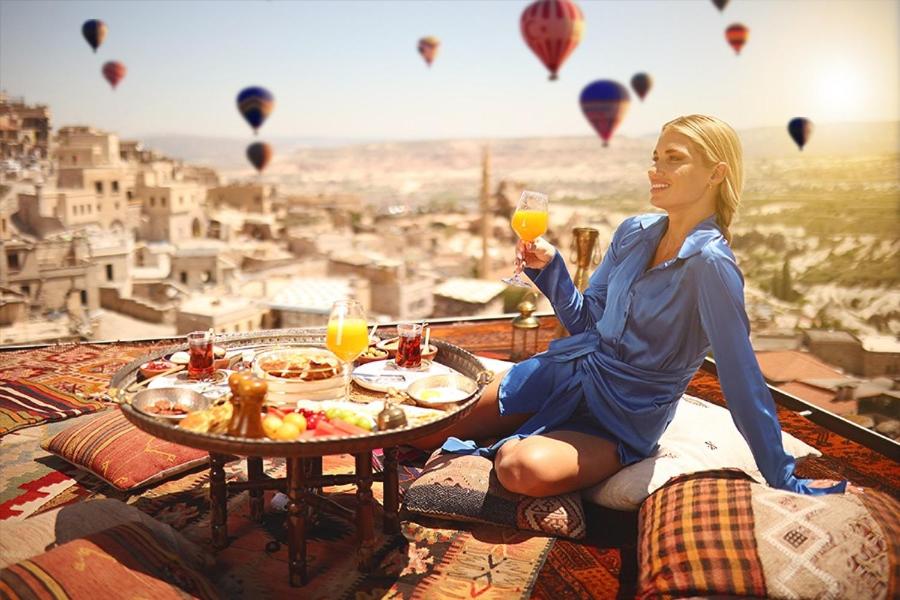 a woman sitting at a table with a glass of wine with hot air balloons at Mak's Cave House in Uchisar