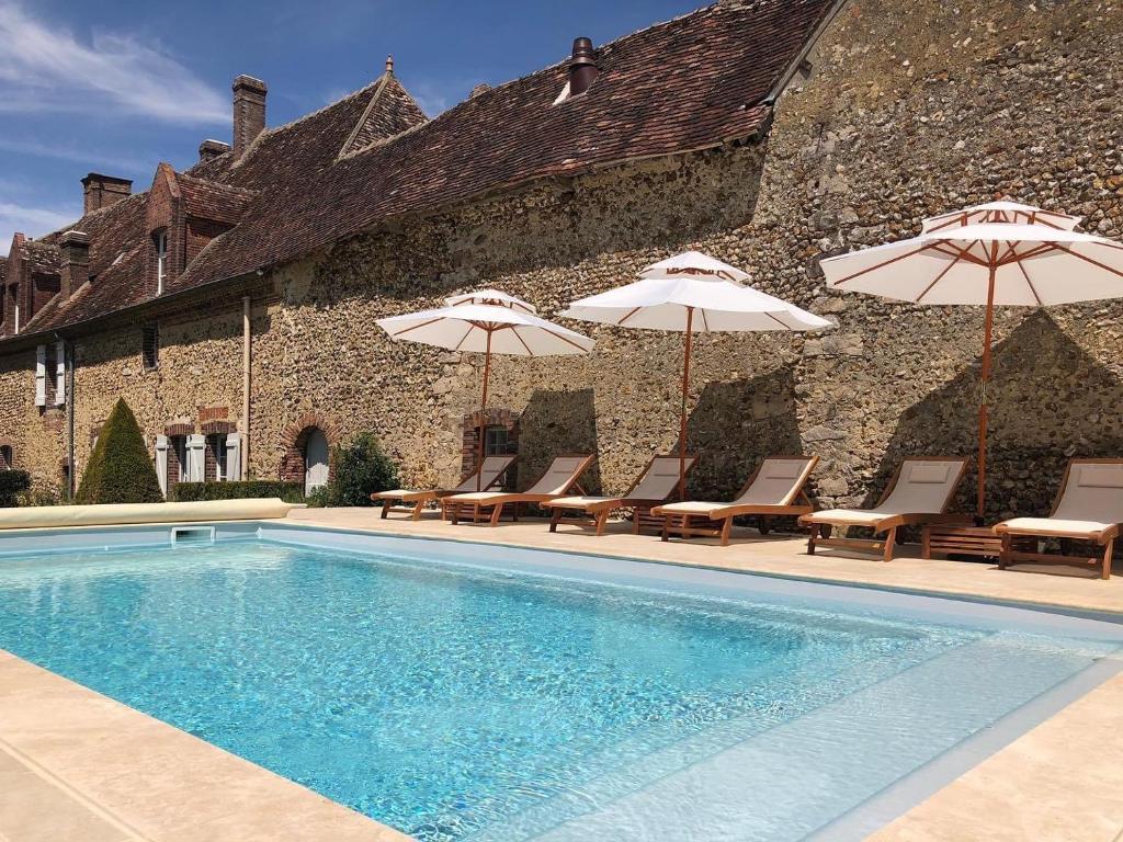 a swimming pool with chairs and umbrellas next to a building at Maison d'hôtes le Prieuré du Preux 