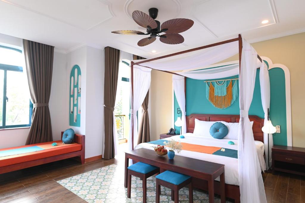 a bedroom with a canopy bed and a desk at De'Colore Villa Hoi An in Hoi An