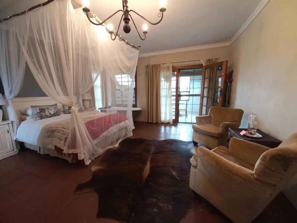 a bedroom with a bed and two chairs and a chandelier at DeKotzenhof in Wakkerstroom