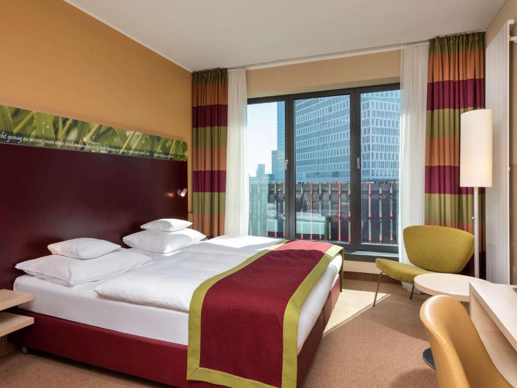 a hotel room with a bed and a large window at Mövenpick Hotel Frankfurt City Messe in Frankfurt