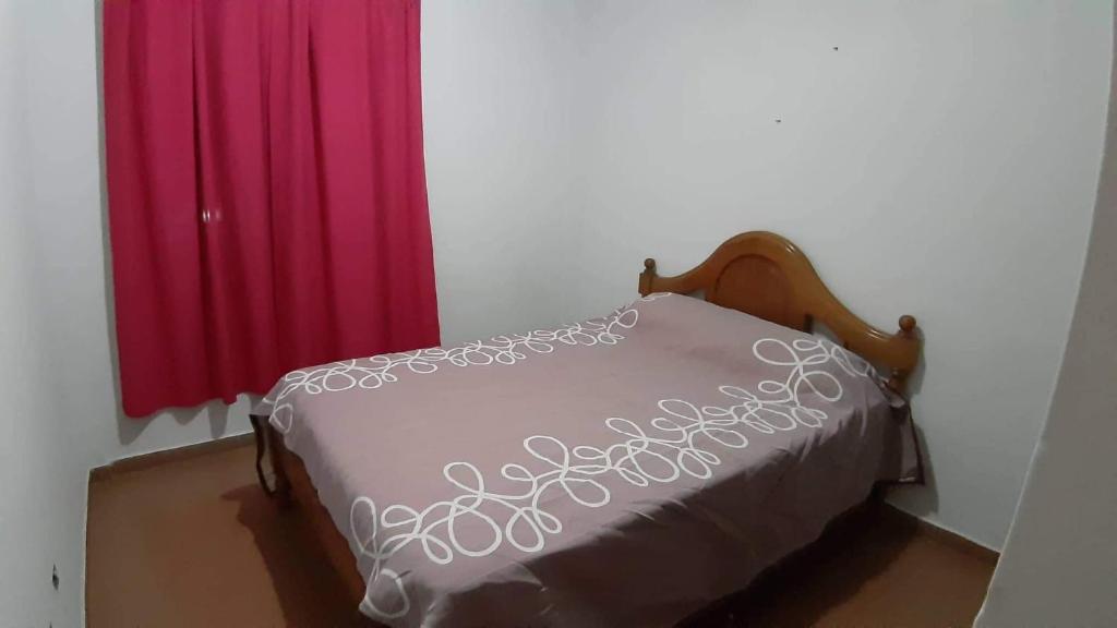 Cama en habitación con 2 cortinas rojas en Las heras en Villa Carlos Paz