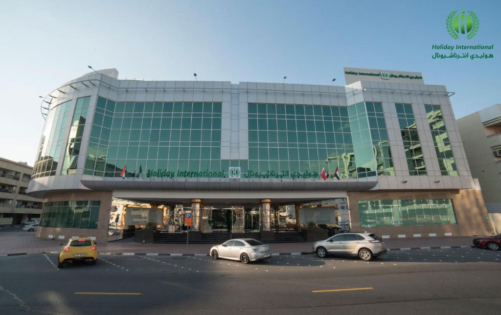 a large building with cars parked in a parking lot at Holiday International Hotel Embassy District in Dubai