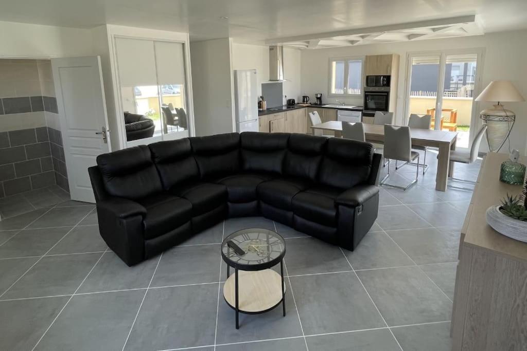 uma sala de estar com um sofá preto e uma cozinha em Maison neuve proche de la mer em Créances