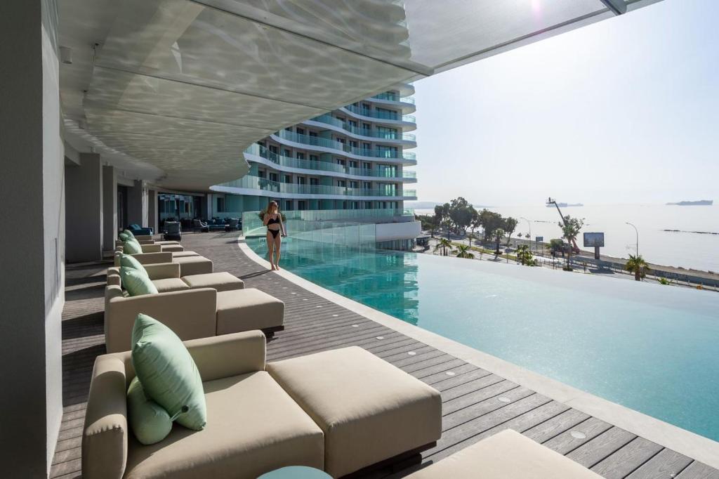 a man standing next to a swimming pool next to a building at Limassol Del Mar in Limassol