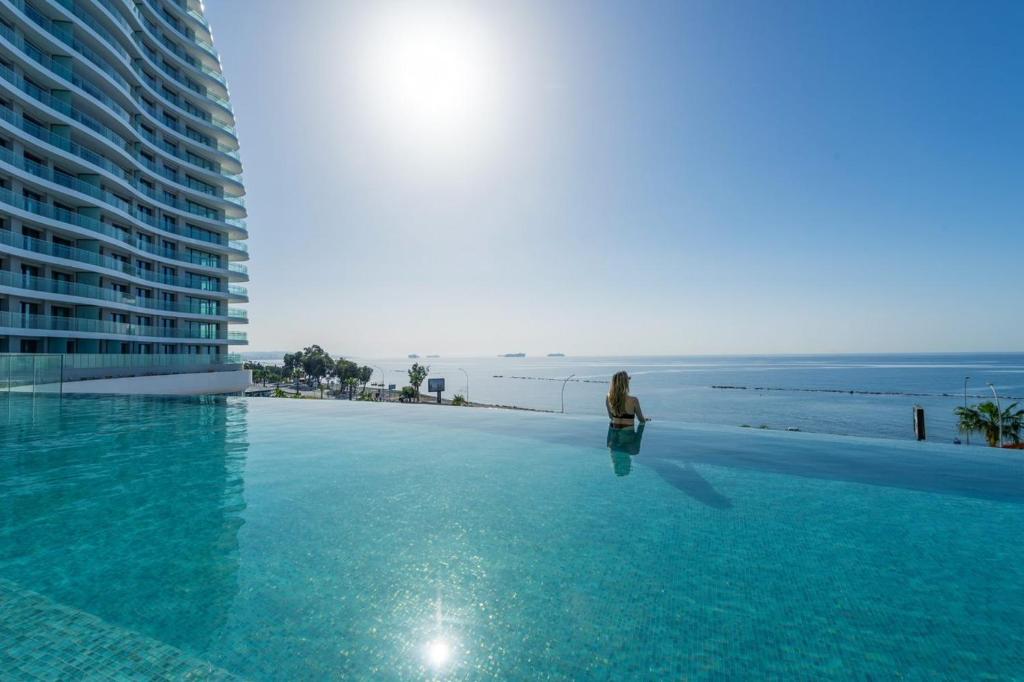 a woman standing on the edge of a swimming pool next to the ocean at Limassol Del Mar in Limassol