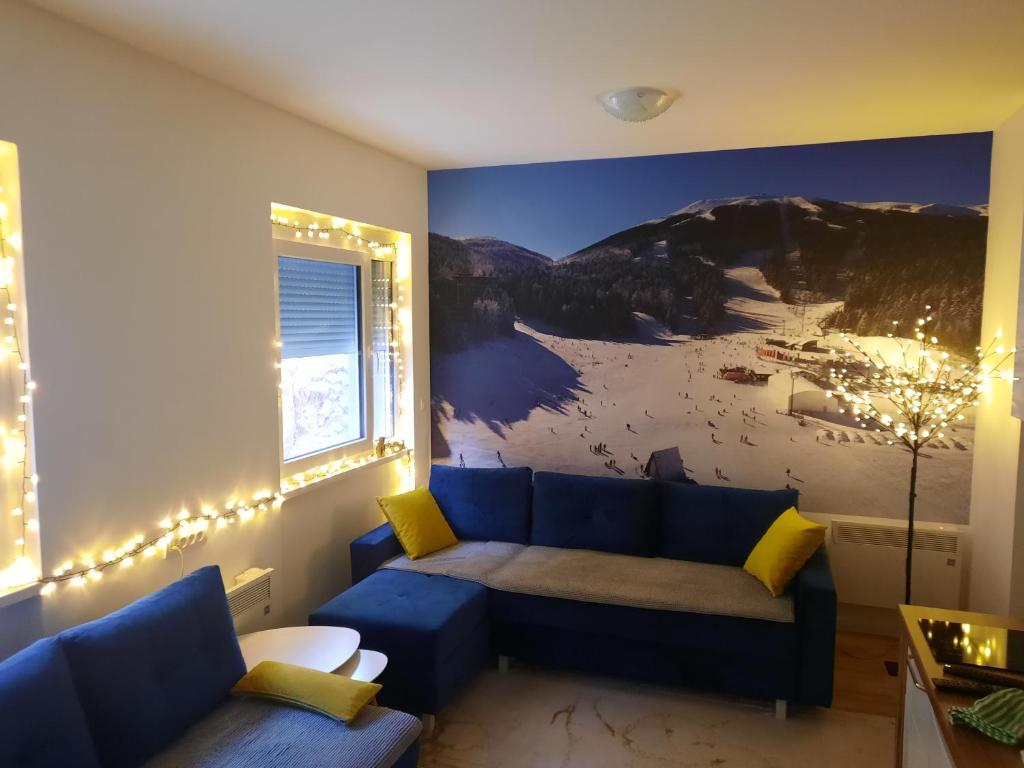 a living room with a blue couch and a mountain mural at Apartman White Wings Bjelasnica in Bjelašnica