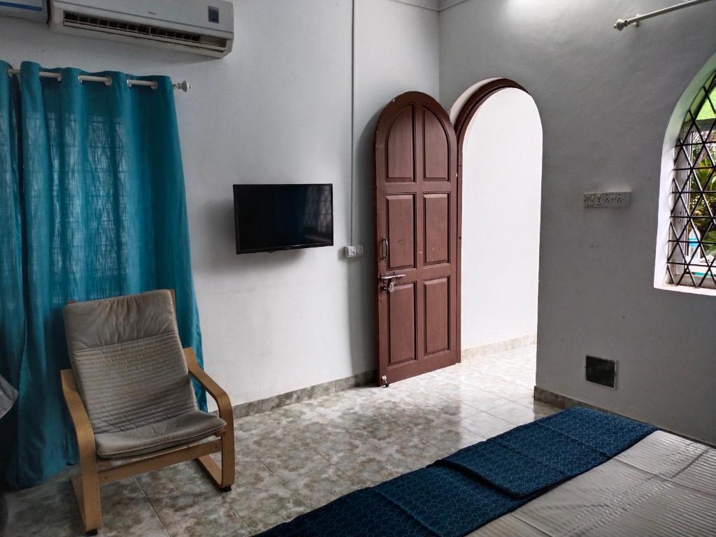 a room with a door and a chair and a television at Rosetta Guesthouse in Anjuna