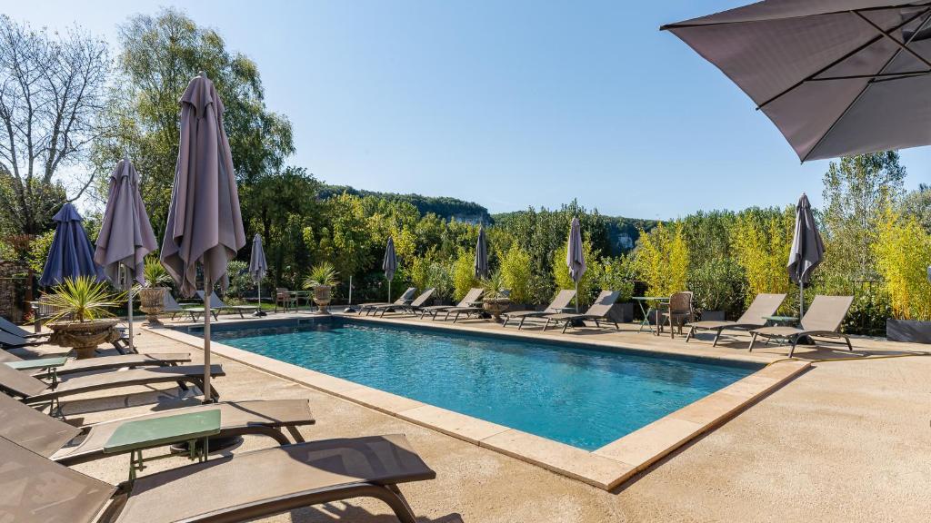 a swimming pool with lounge chairs and umbrellas at Hostellerie du Passeur - Hôtel & Restaurant - Climatisation et Piscine chauffée in Les Eyzies-de-Tayac