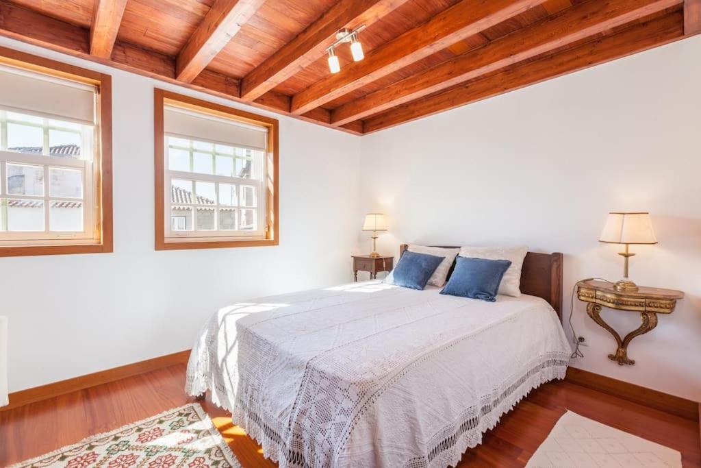 a white bedroom with a bed and two windows at Apartamentos Lumar in Valença