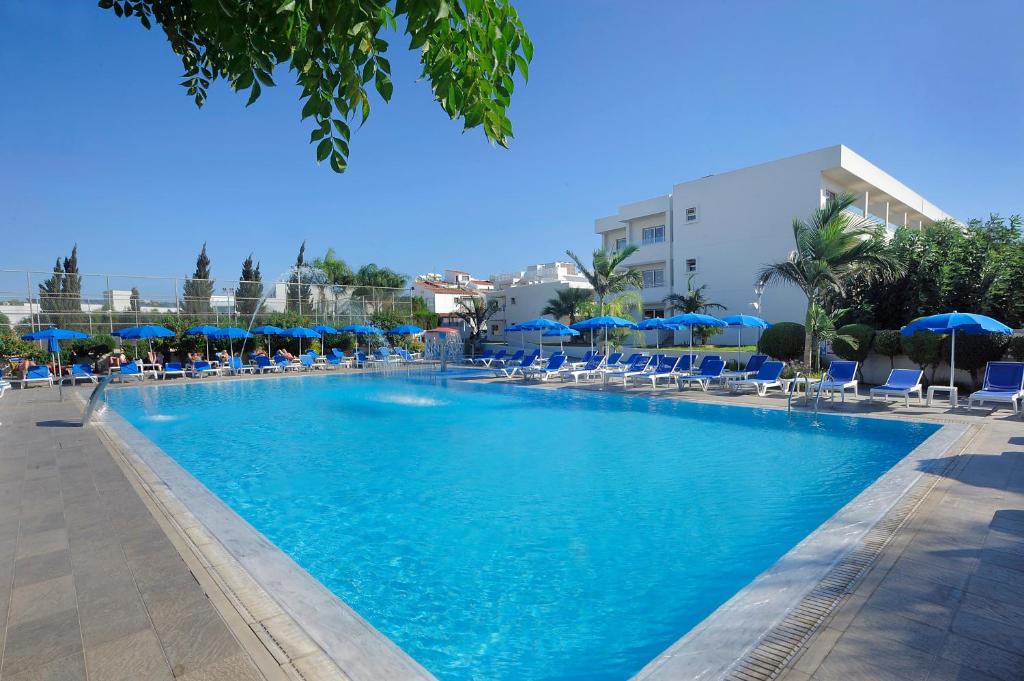 ein großer Pool mit Stühlen und blauen Sonnenschirmen in der Unterkunft Euronapa Hotel Apartments in Ayia Napa