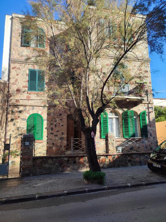 a tree in front of a building with green shutters at Villa catalana al centro di Alghero in Alghero