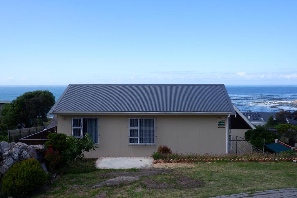 a small white house with the ocean in the background at Aloe Ocean Flatlet in Bettyʼs Bay