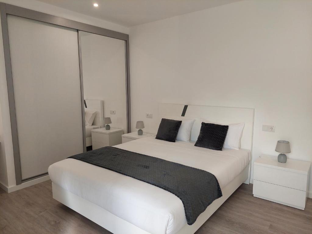 Dormitorio blanco con cama blanca grande y almohadas negras en Apartment Til en Funchal