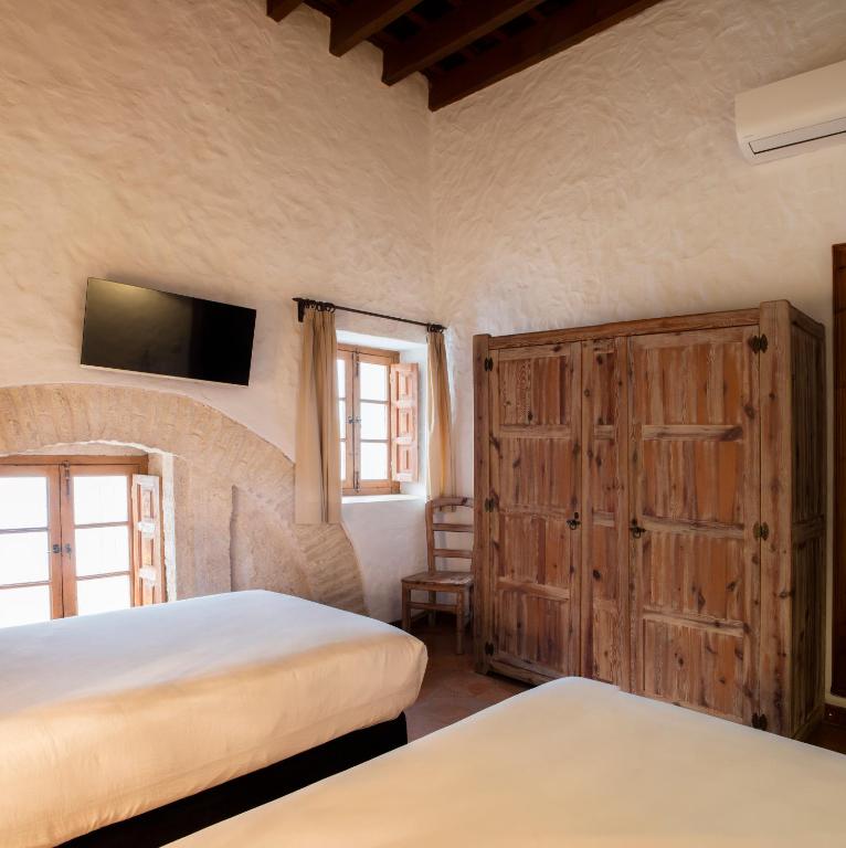 a bedroom with two beds and a tv on the wall at Hotel Tugasa Convento San Francisco in Vejer de la Frontera