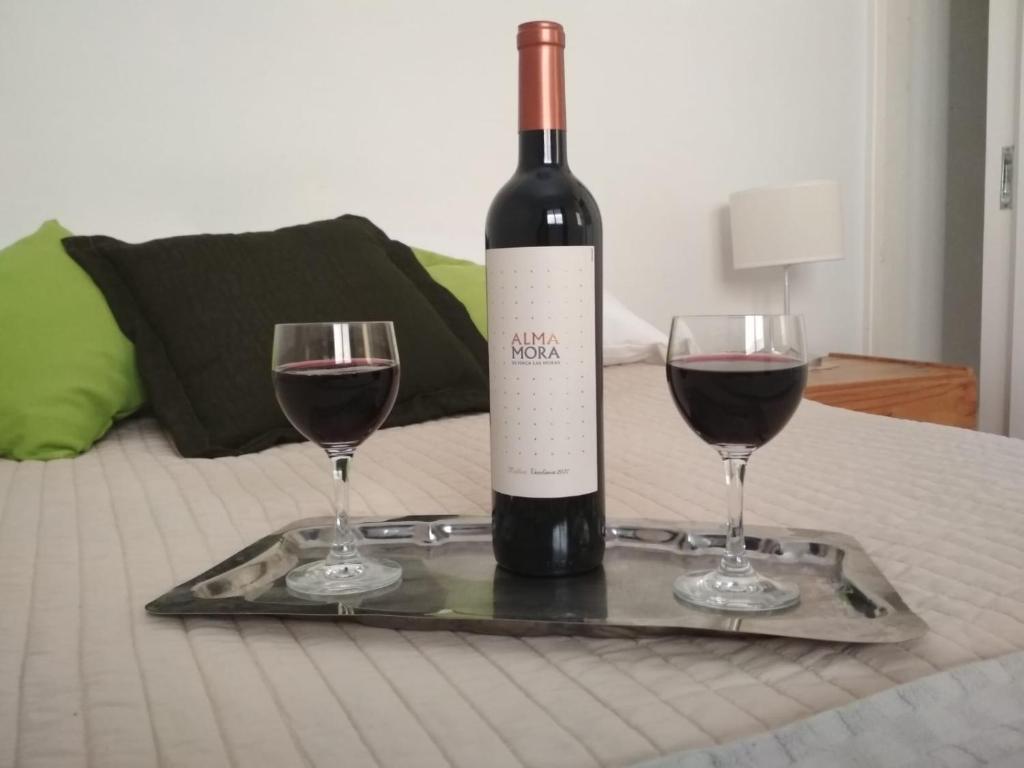 Una botella de vino y dos copas en una cama. en NUESTRO DEPARTAMENTO en Godoy Cruz