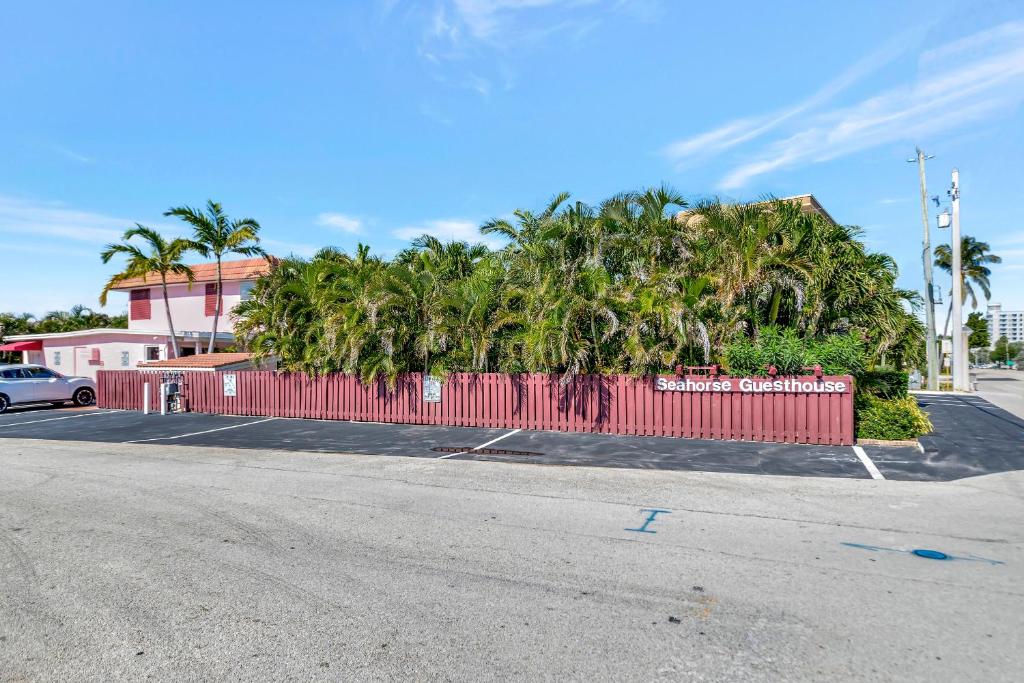 a red fence in front of a parking lot with palm trees at Seahorse Guesthouse in Pompano Beach