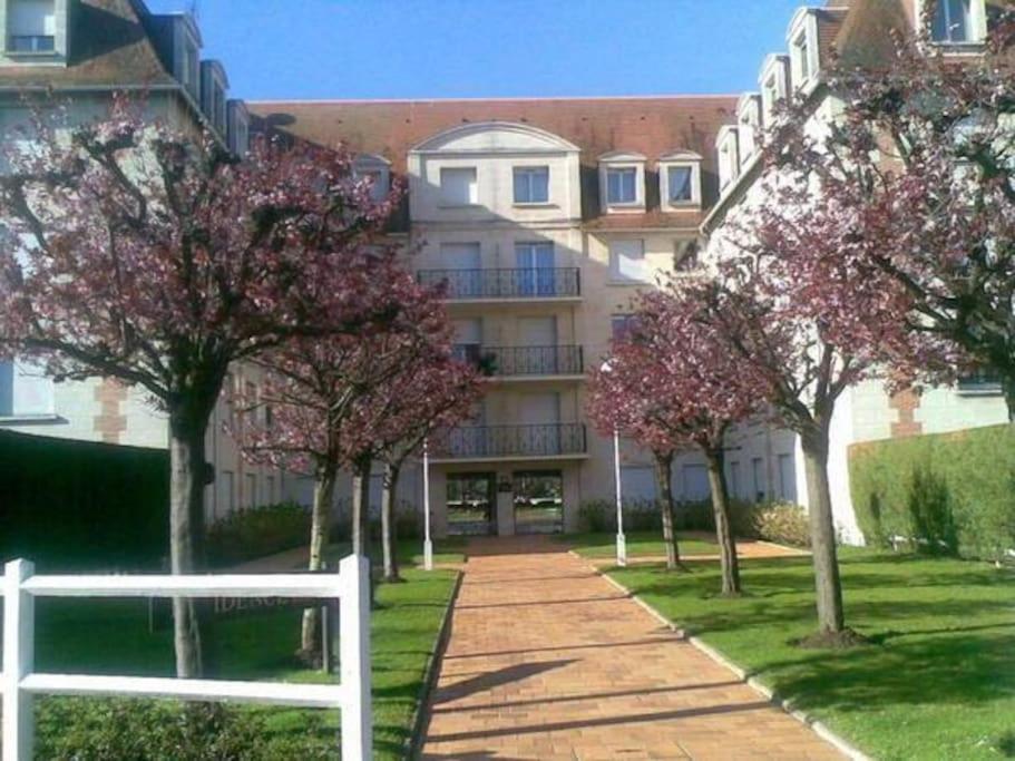 un bâtiment avec des arbres devant lui et une clôture blanche dans l'établissement Sevigné Plage, à Deauville