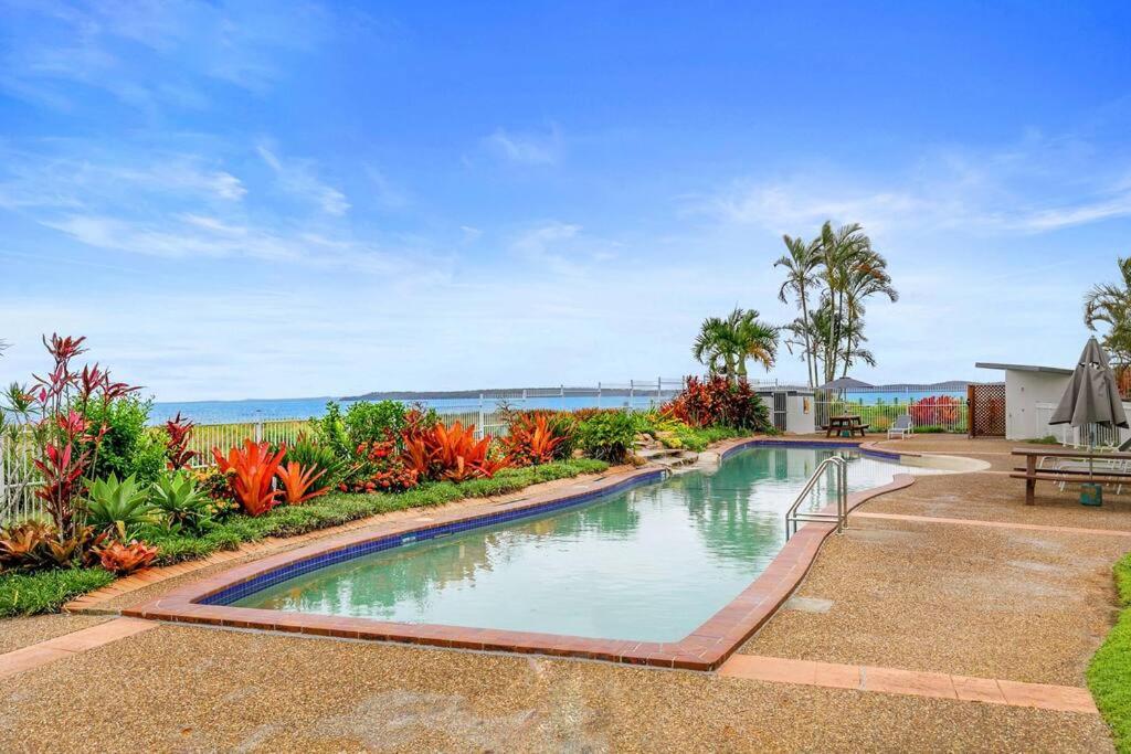 a swimming pool in a garden with the ocean in the background at Luxury Beach Front Apartment in Urangan