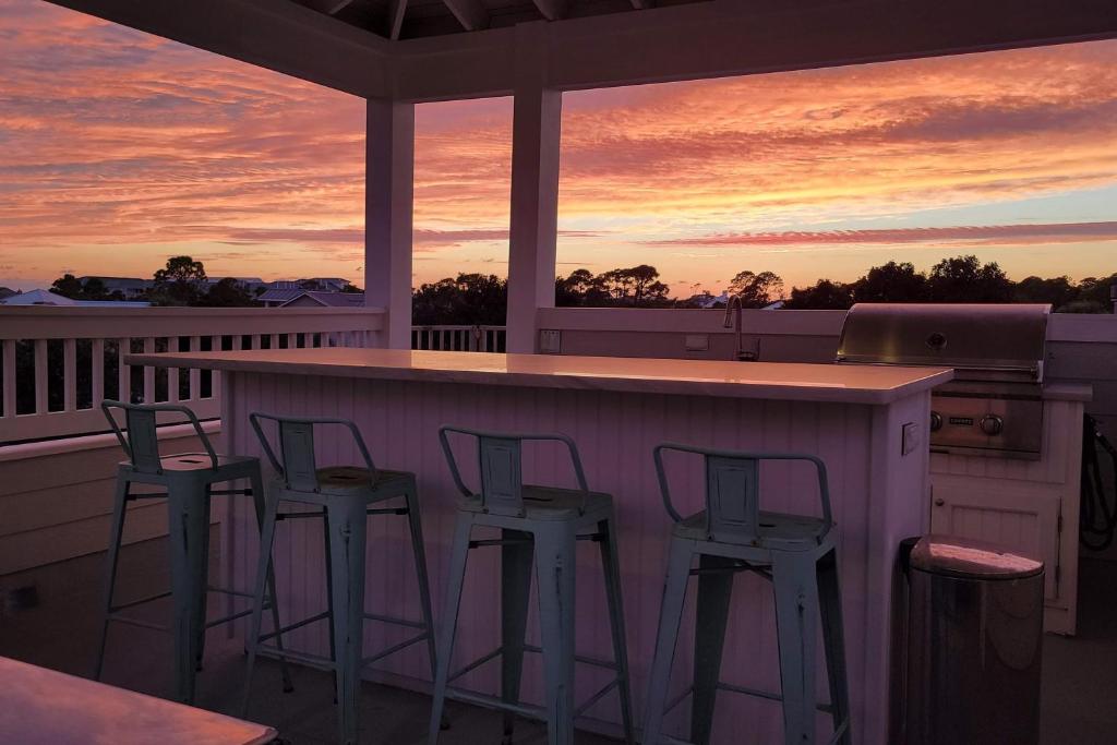 Un porche con una barra con taburetes y una puesta de sol. en Golf Cart, 3 King Beds, Covered Rooftop Area, Half Mile to Beach!, en Santa Rosa Beach