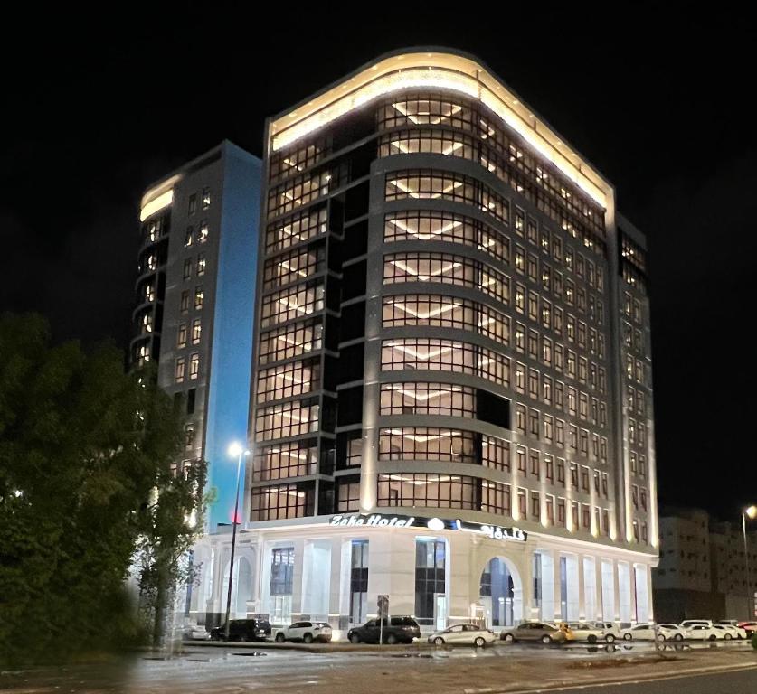 Zaha Taiba Hotel في المدينة المنورة: مبنى كبير في الليل مع سيارات متوقفة أمامه