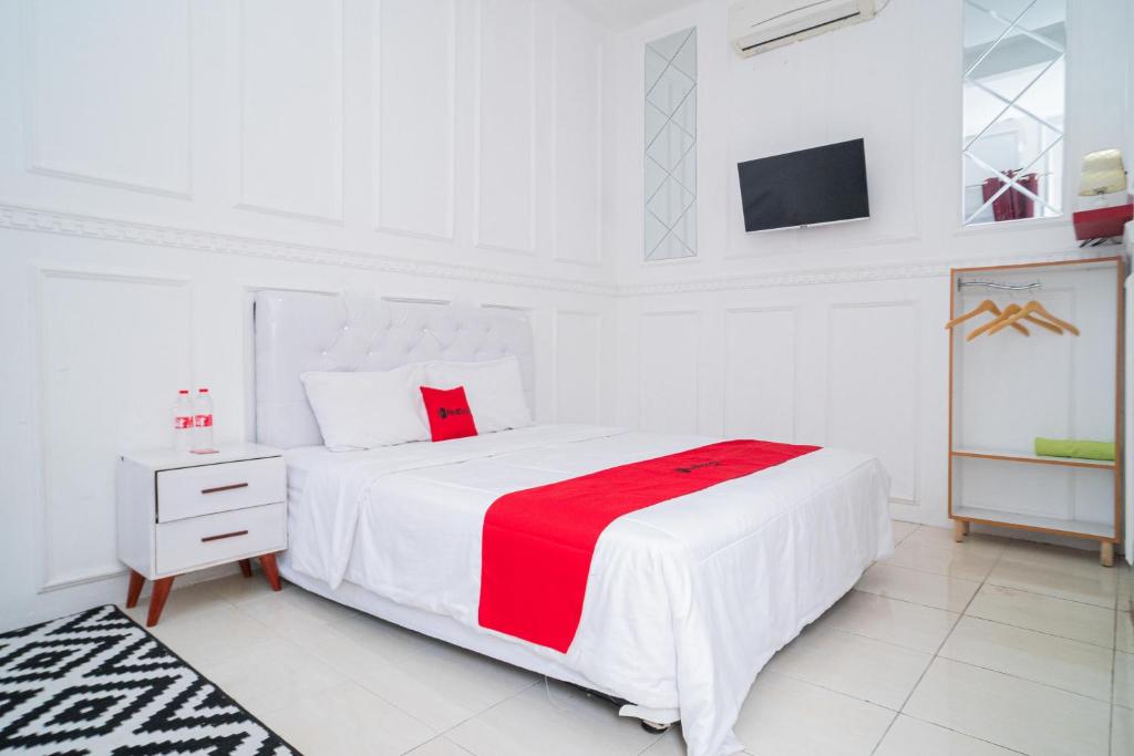 um quarto branco com uma grande cama branca com um cobertor vermelho em RedDoorz Syariah at Aura Homestay em Ponorogo
