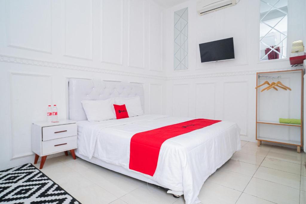 a white bedroom with a large white bed with a red blanket at RedDoorz Syariah at Aura Homestay in Ponorogo