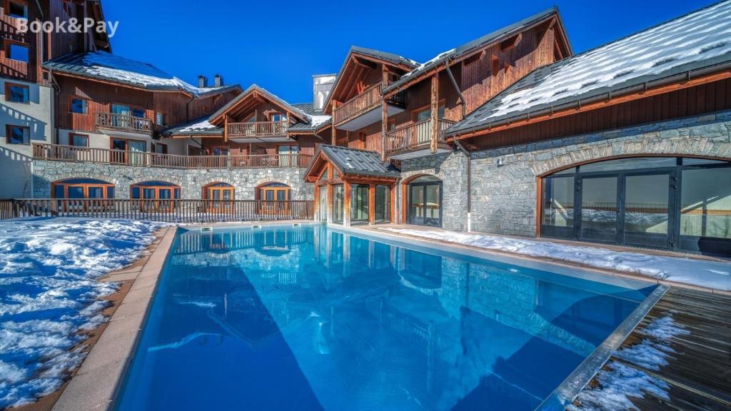 a swimming pool in front of a building with snow on the ground at Les Alpages du Corbier A102 in Villarembert