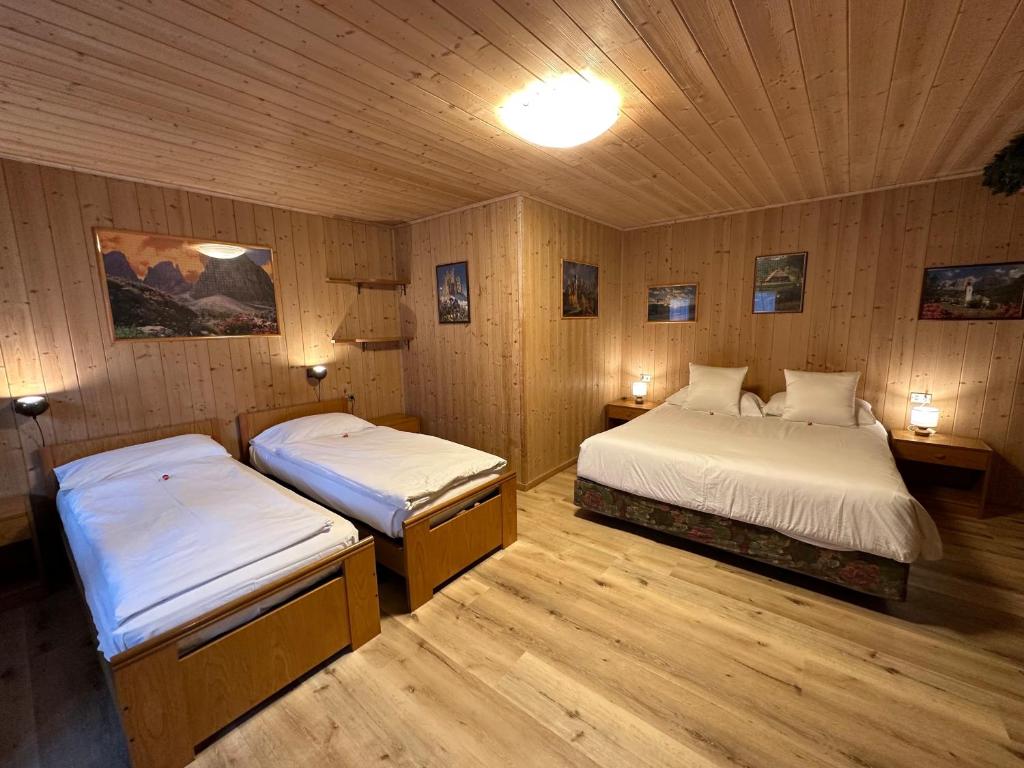 two beds in a room with wooden walls at B&B Family Accommodation Canazei BIKE FRIENDLY in Canazei