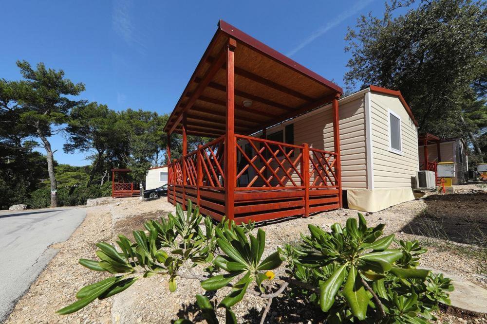 uma pequena cabana com um corrimão vermelho e um alpendre em Mobile homes in Camp Soline at Biograd, with sand- and pebble beach em Biograd na Moru