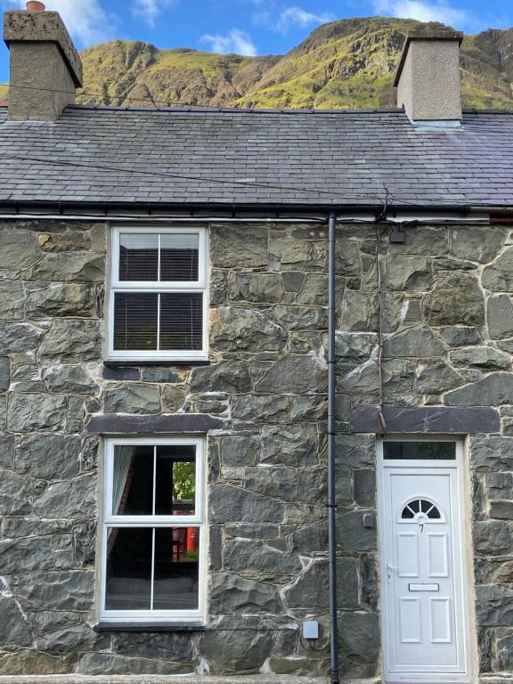 uma casa de pedra com duas janelas e uma porta branca em Ty'n y Cwm, Nant Peris em Dinorwic