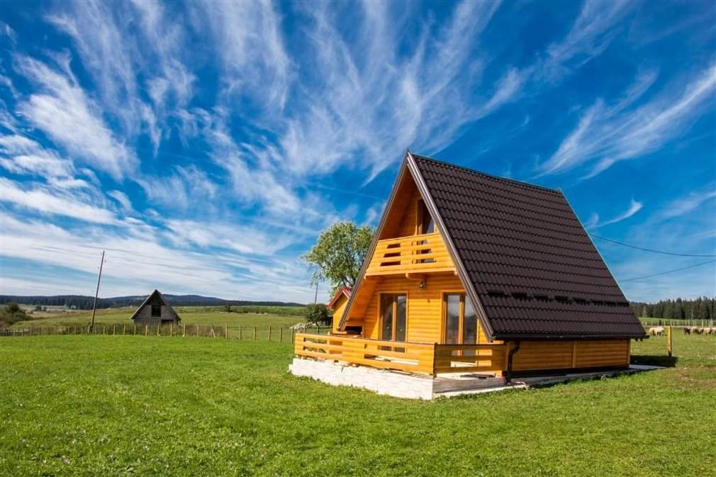 Han Pijesak的住宿－ROMANIJA - Brvnara za odmor，一座木房子,在田野上设有黑色屋顶