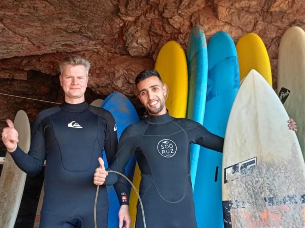 two men in wet suits standing in front of surfboards at Dar diafa samira in Mirleft