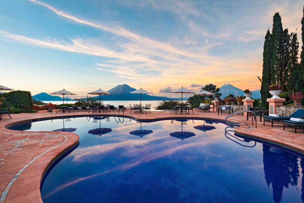 a large swimming pool with umbrellas and a sunset at Hotel Atitlan in Panajachel