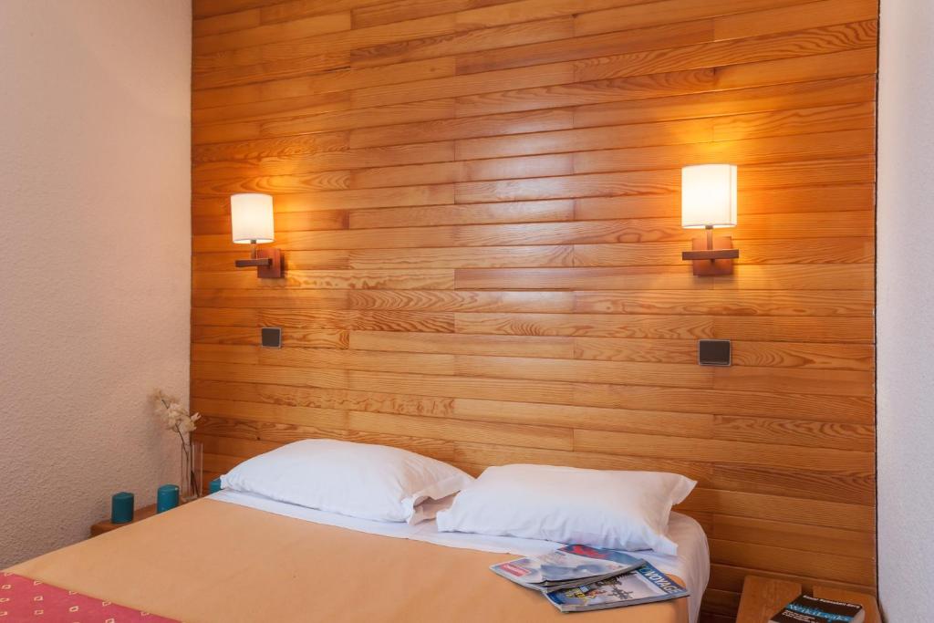a bed with two pillows and two lights on a wooden wall at Résidence Pierre &amp; Vacances Emeraude in Belle Plagne