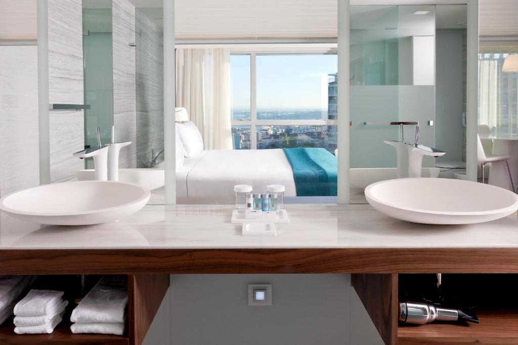 A double-sink vanity looking through glass toward the bedroom and city view.