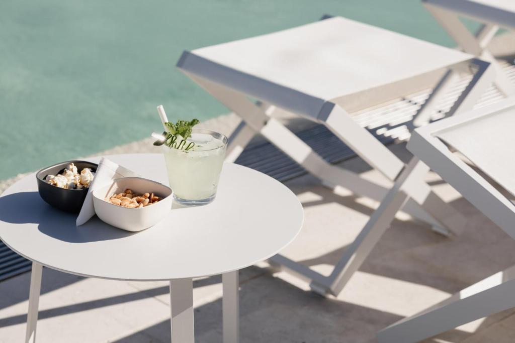 A poolside table set with popcorn, snacks, and a chilled drink beside white loungers.