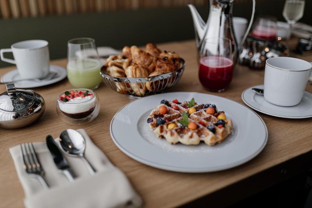 A plated breakfast spread with waffles, pastries, fruit, drinks and coffee.