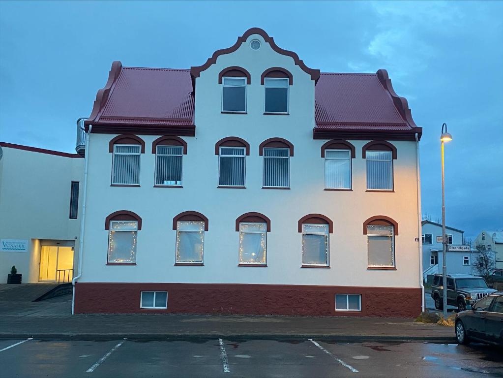 a white building with a red roof in a parking lot at Hrimland Guesthouse in Akureyri