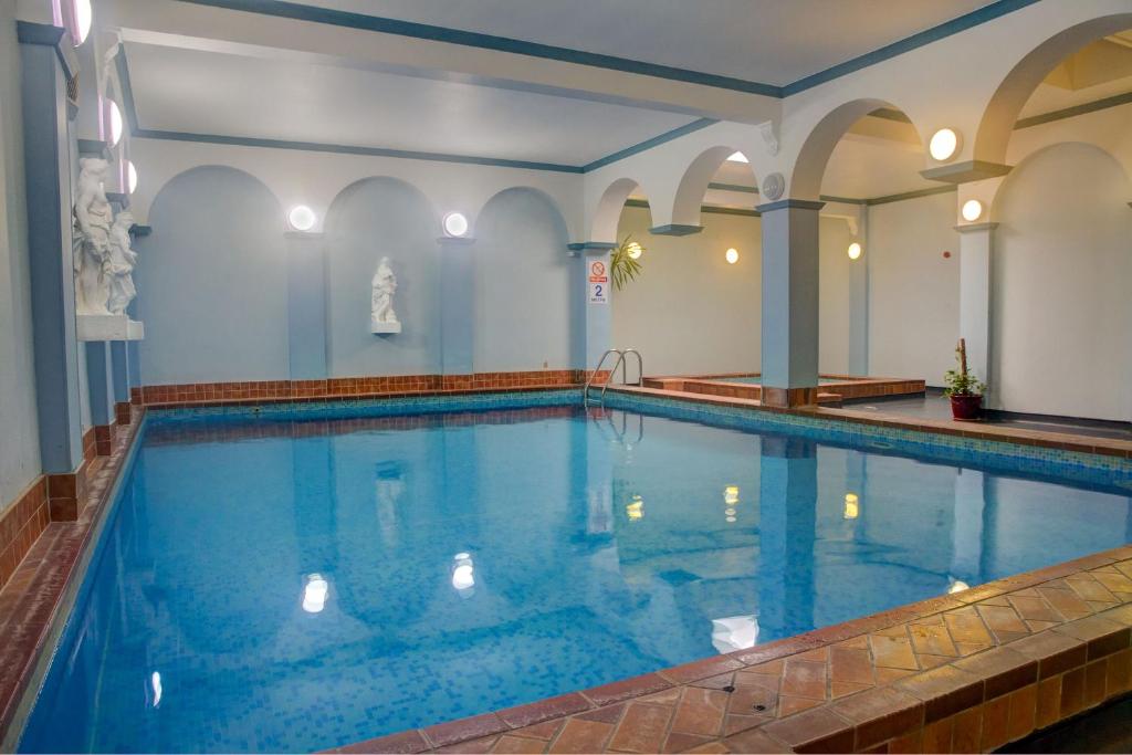 a large swimming pool with blue water in a building at Chatsworth House Hotel in Llandudno