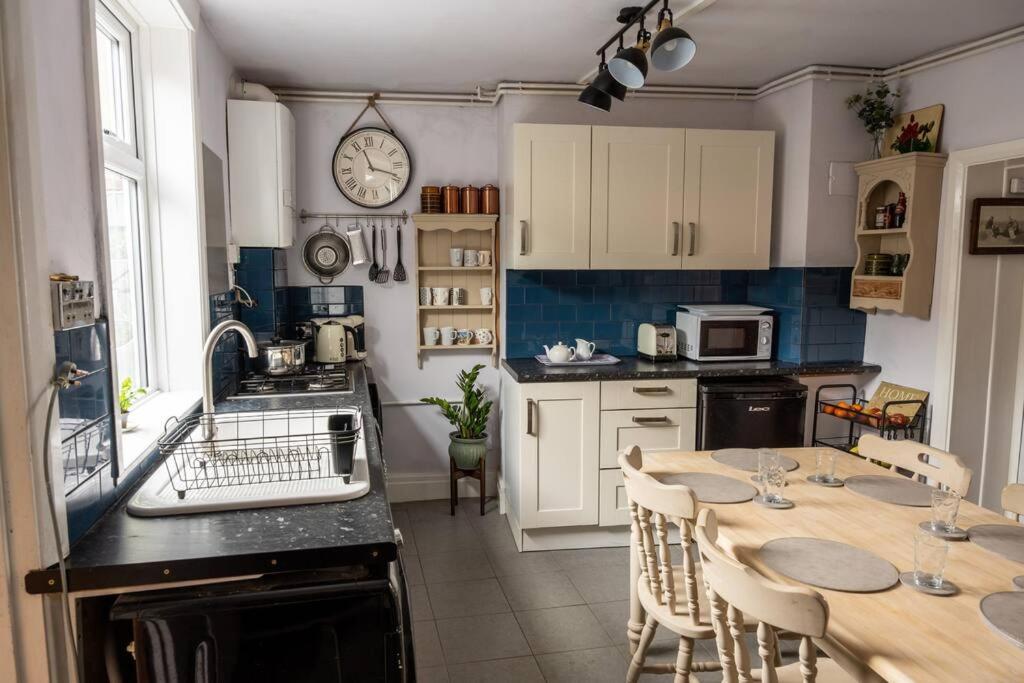 a kitchen with a table and a clock on the wall at Spacious Charming Cottage near Lake and Sea in Hornsea