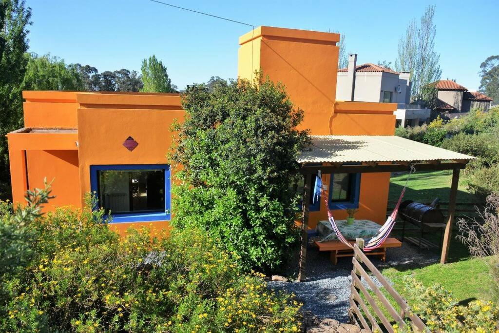 una pequeña casa naranja con banco y porche en La Salamandra. Casa en la Sierra en Tandil