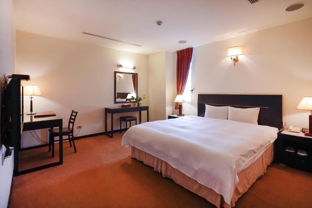 a hotel room with a large white bed and a desk at Herkang Hotel in Taichung