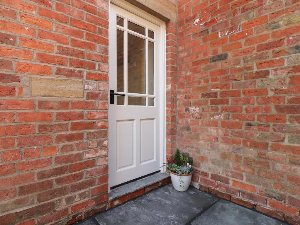 uma porta branca numa parede de tijolos com um vaso de plantas em The Byre em Preston
