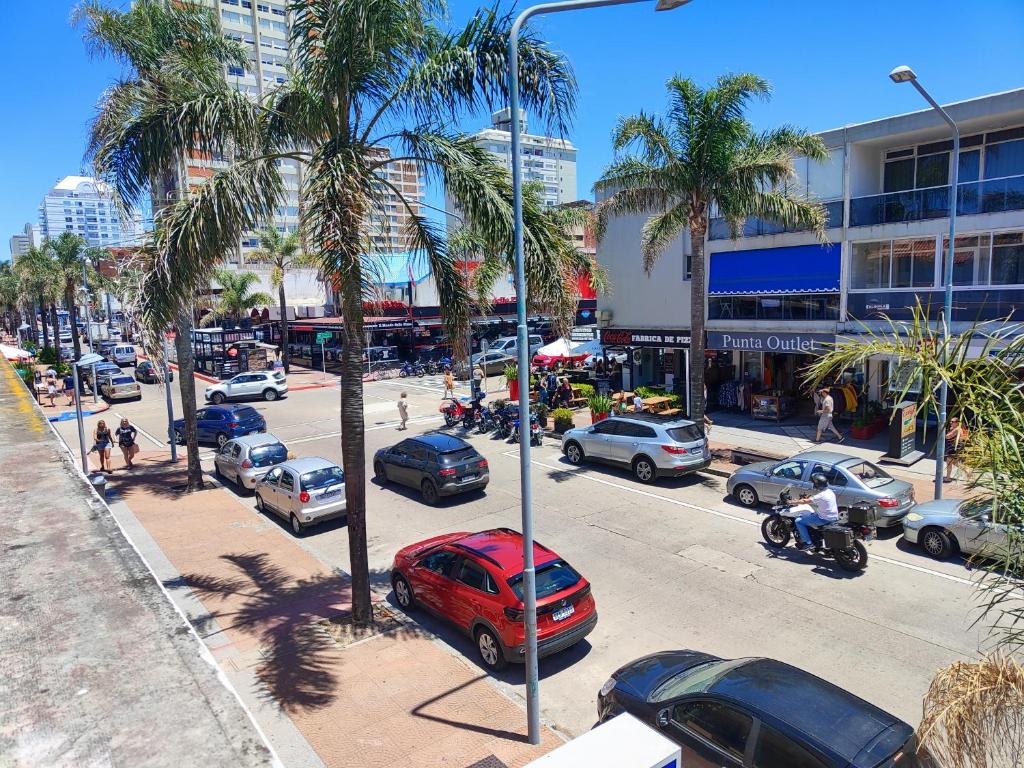 una concurrida calle de la ciudad con coches aparcados y palmeras en Apartamento sobre Gorlero, en Punta del Este