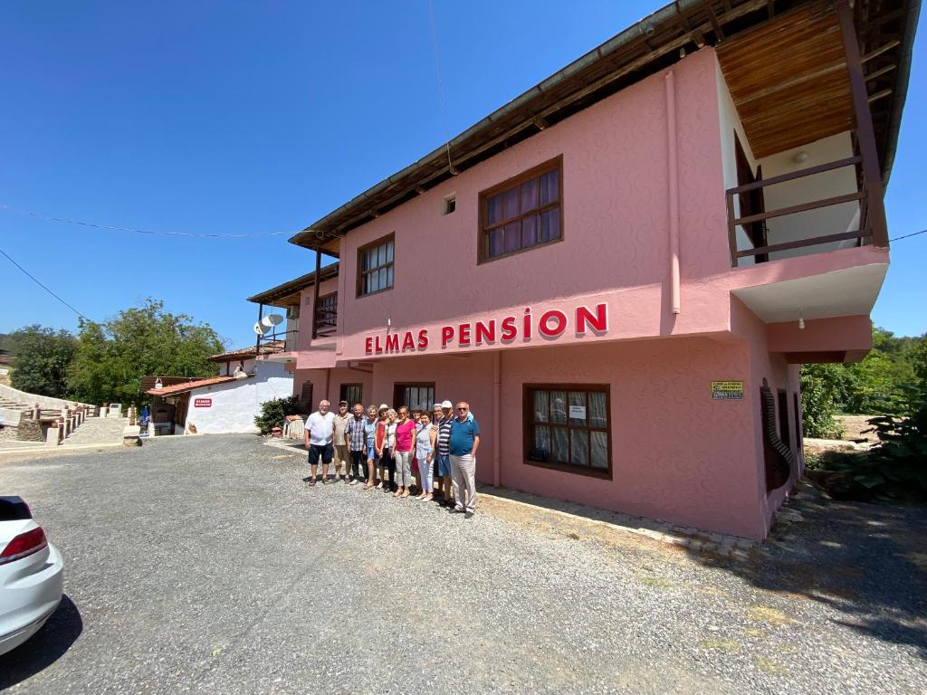 un groupe de personnes debout devant un bâtiment rose dans l'établissement Elmas Pansiyon, à Karacasu