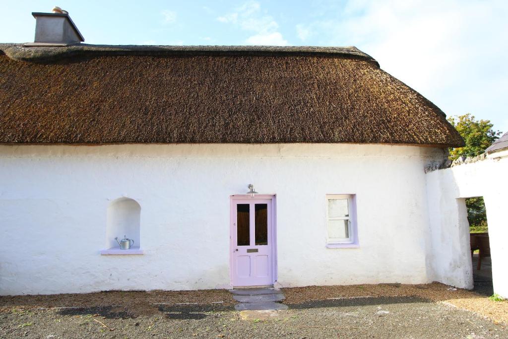 un edificio blanco con techo de paja y puerta morada en Hailey's Haven en Dungarvan